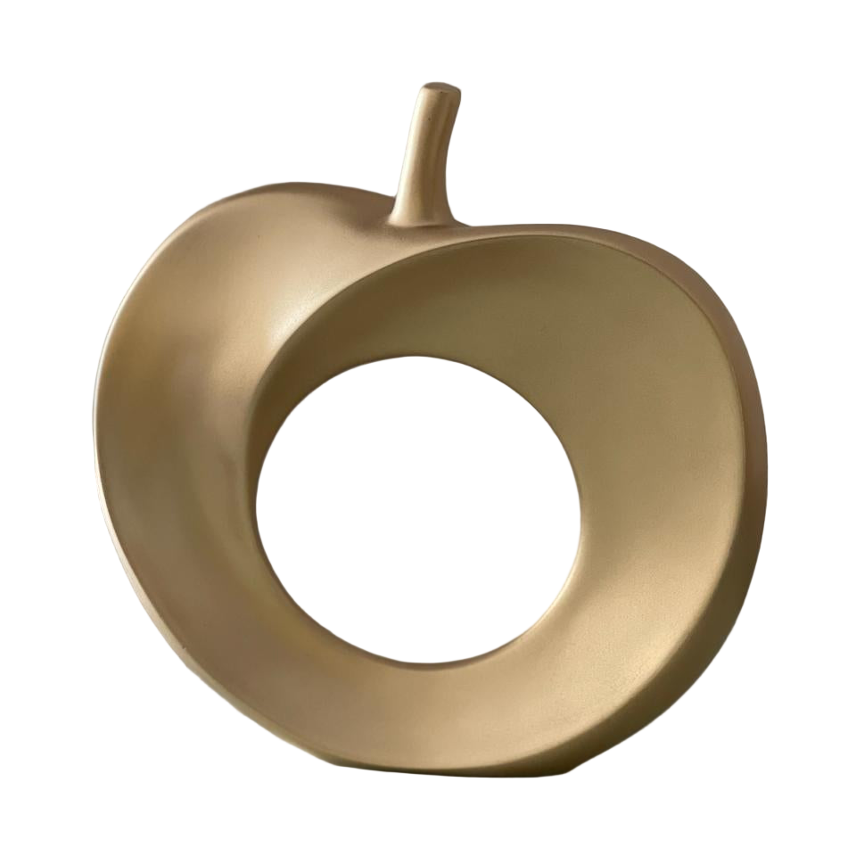Gold decorative object resembling an apple on a reflective surface with a neutral background
