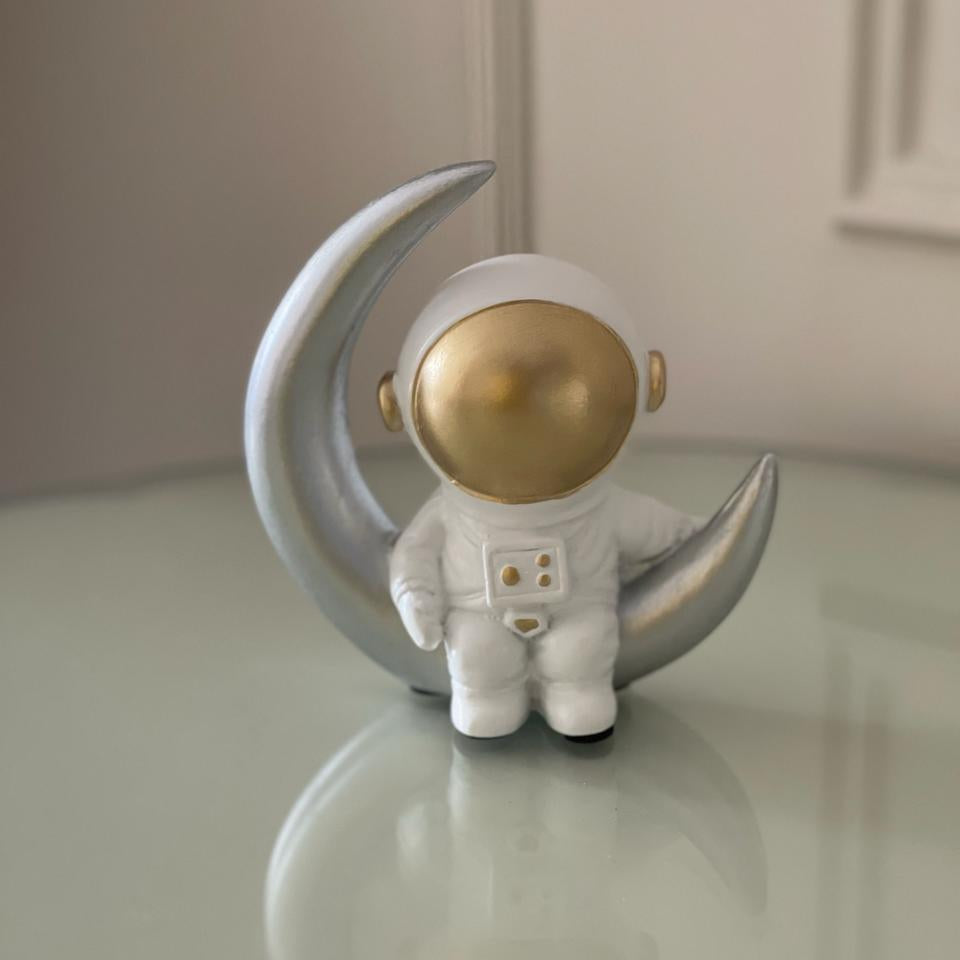 Decorative figurine of an astronaut on a moon-shaped stand with a neutral background