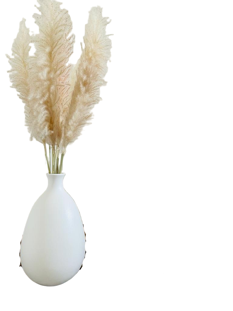 White vase with pampas grass next to a brown knitted blanket on a wooden floor.