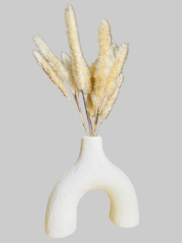 White textured vase with dried pampas grass on a table in a living room setting.