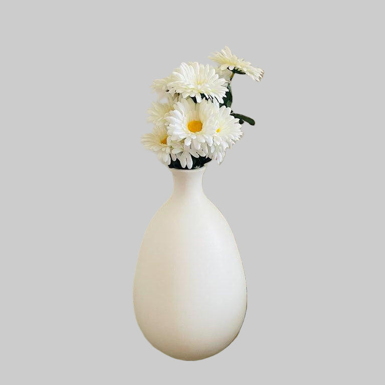 White vase with flowers on a glass table against a beige curtain.