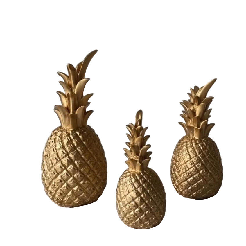 Three gold pineapple decorations on a textured surface with a neutral background