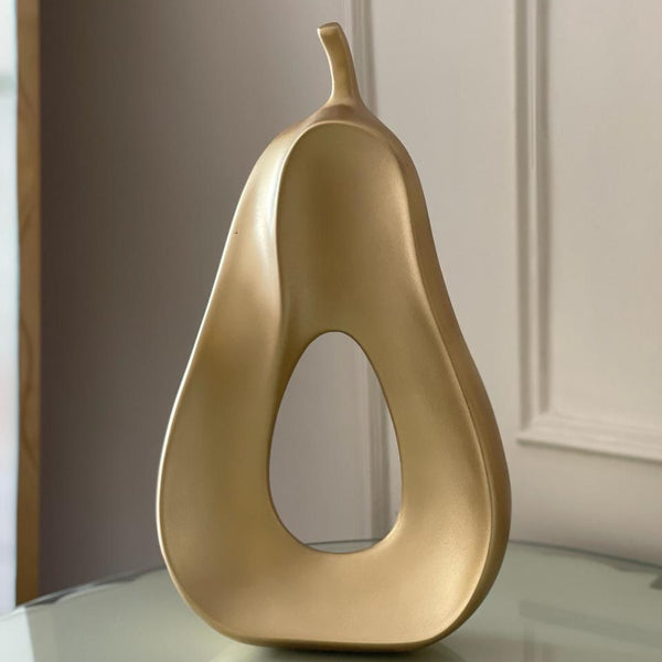 Gold pear-shaped decorative object on a reflective surface with a neutral background