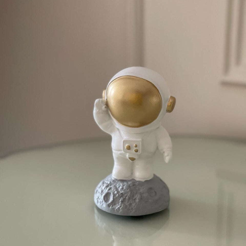 Small figurine of an astronaut with a gold helmet on a gray base, set against a neutral background.