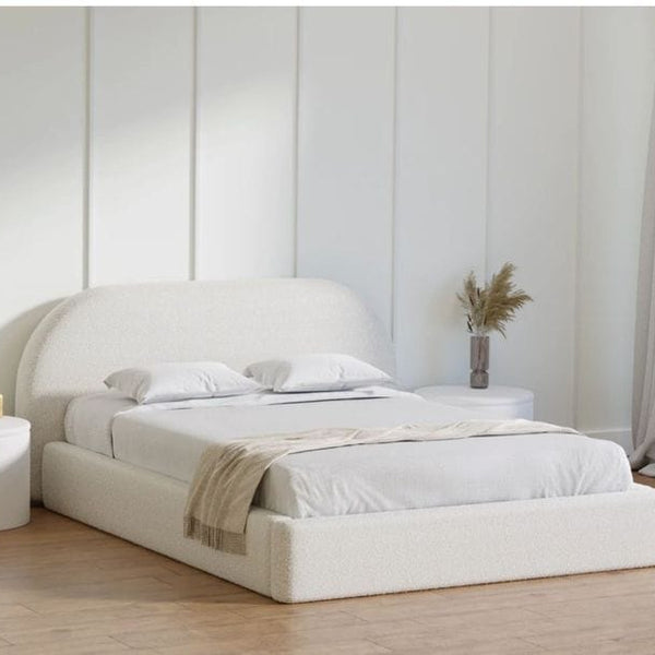 White upholstered bed in a minimalistic bedroom with light wood flooring and white walls.