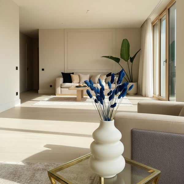 Modern living room with a vase of blue flowers on a glass table.