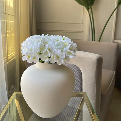 White vase with flowers on a glass table in a room with a chair and decorative elements.
