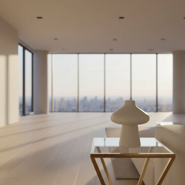 White vase on a glass table with a plant in the background