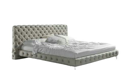 Modern bedroom with a gray tufted bed and white drapes.