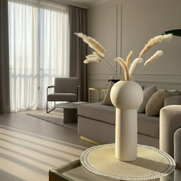 Decorative vase with dried plants on a round table in a living room setting.