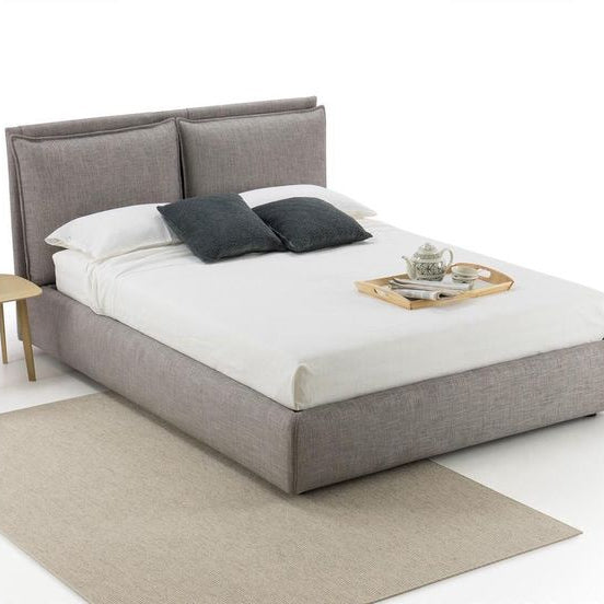 Gray upholstered bed with white bedding and gray pillows on a white background