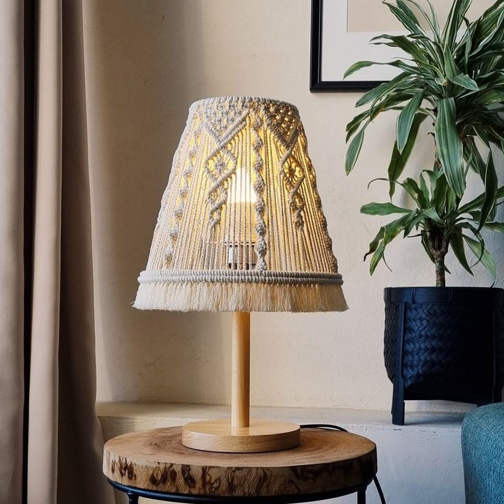 Decorative table lamp with wicker shade on a wooden side table, plant in the background