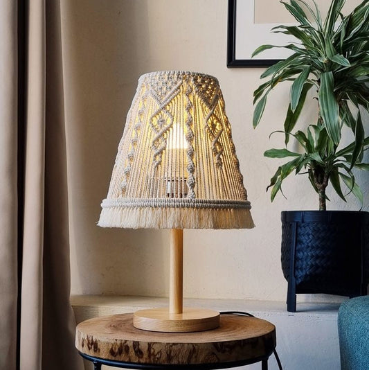 Decorative table lamp with wicker shade on a wooden side table, plant in the background