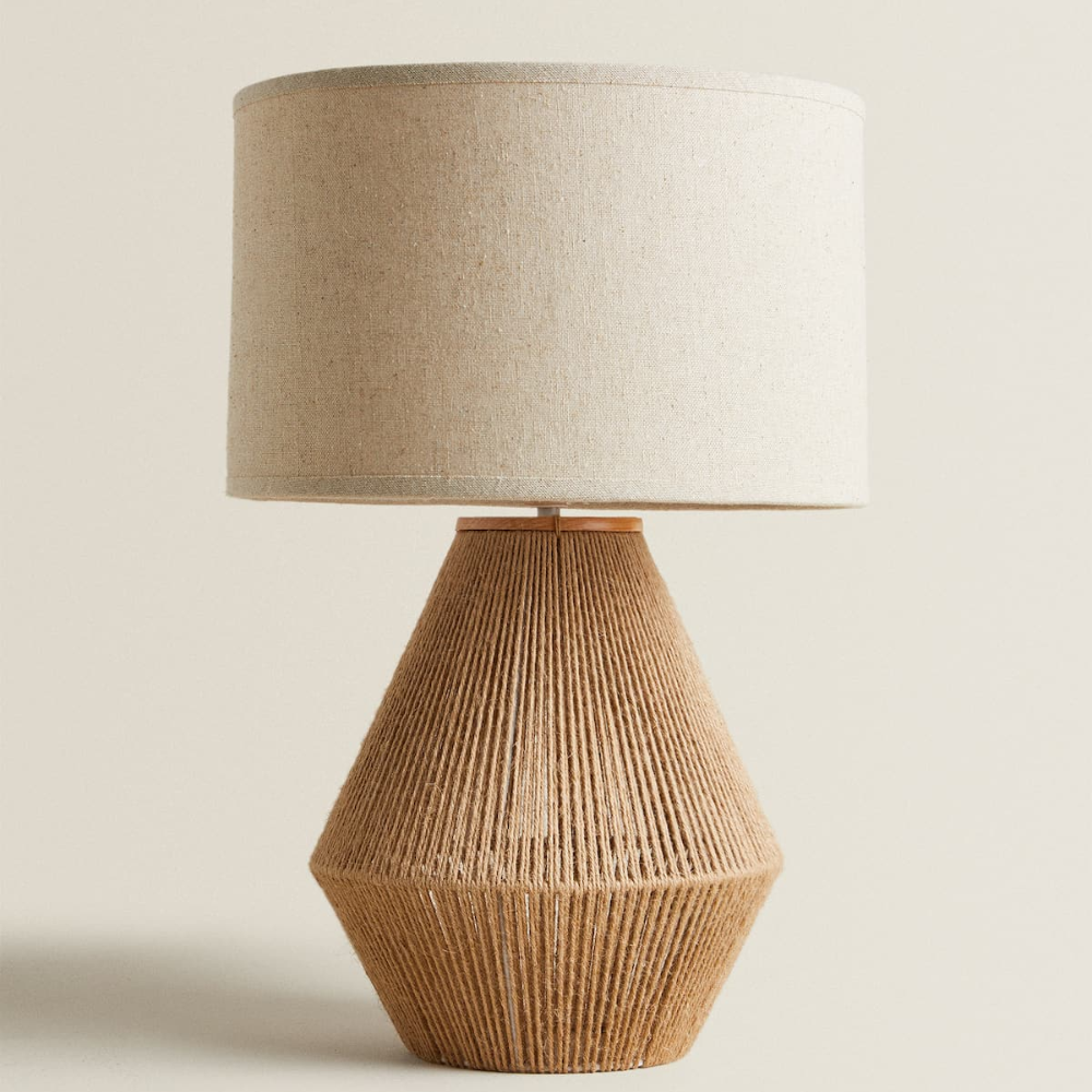Table lamp with woven base and beige fabric shade on a neutral background