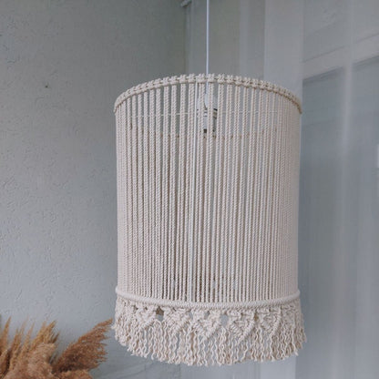 Macrame lampshade hanging against a light gray wall with dried plants.