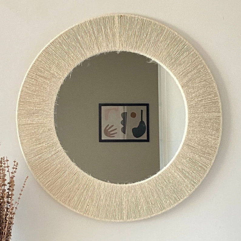Round mirror with a textured beige frame on a white wall