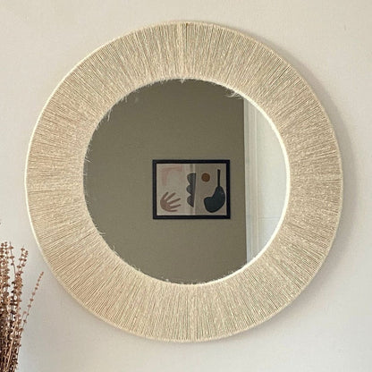 Round mirror with a textured beige frame on a white wall
