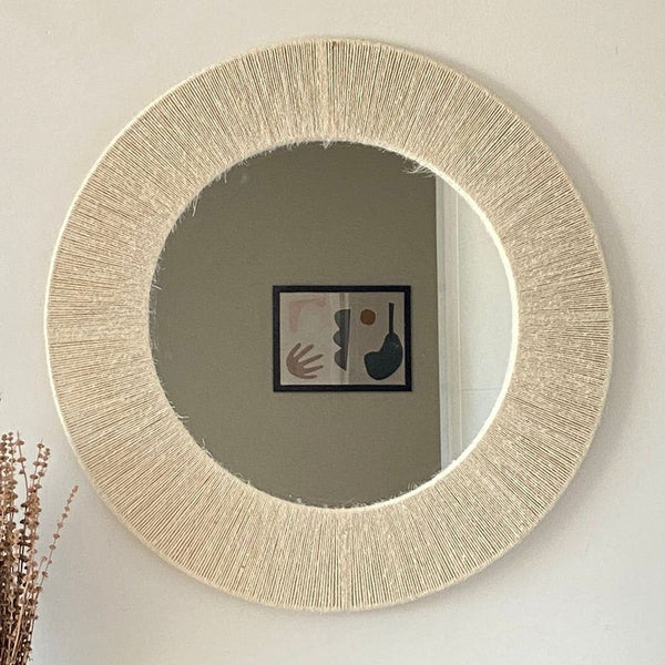 Round mirror with a textured beige frame on a white wall