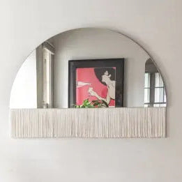 Round mirror with a shelf on a white wall, featuring a framed picture.
