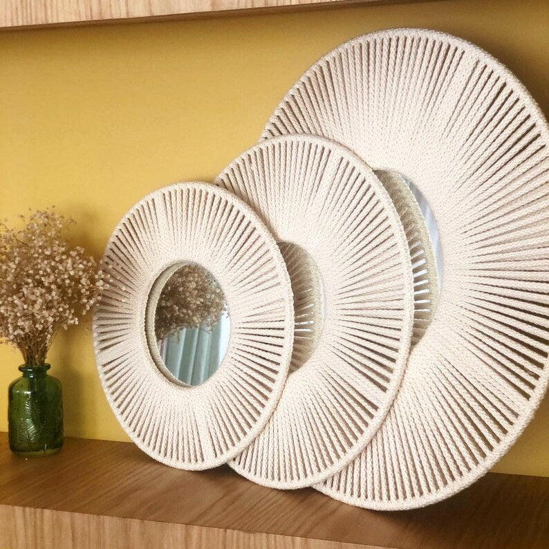 Set of three white woven wall mirrors on a wooden shelf against a yellow wall.