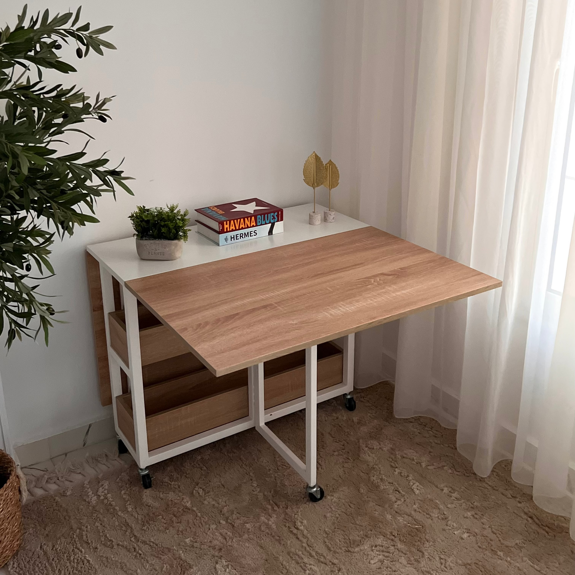 Wooden desk with white top in a room with a plant and curtains.