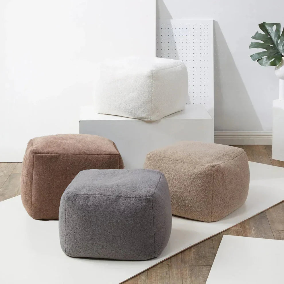 Three cube-shaped ottomans in brown, gray, and beige on a white rug.