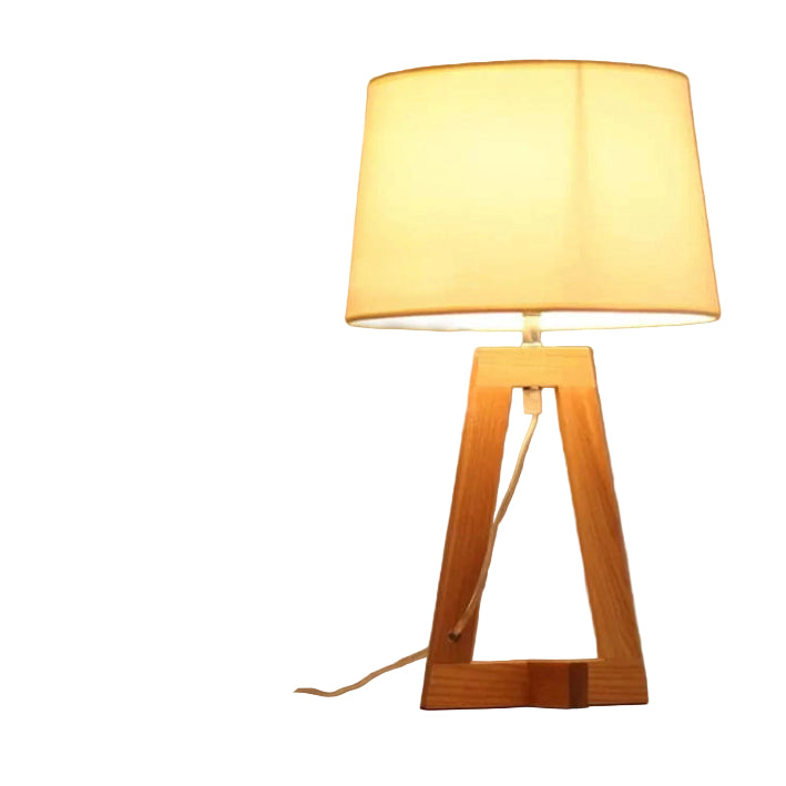 Table lamp with wooden base and white shade on a surface with books and a plant in the background.