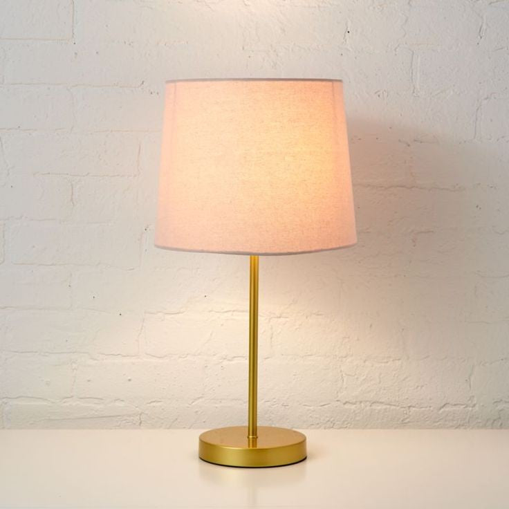 Table lamp with a pink shade and gold base on a white surface with a light gray textured wall background