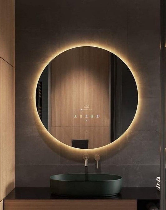 Round illuminated bathroom mirror with a dark sink below on a tiled wall.